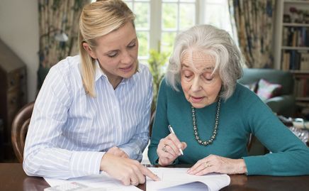 Jüngere Frau unterstützt Seniorin beim Ausfüllen eines Formulars